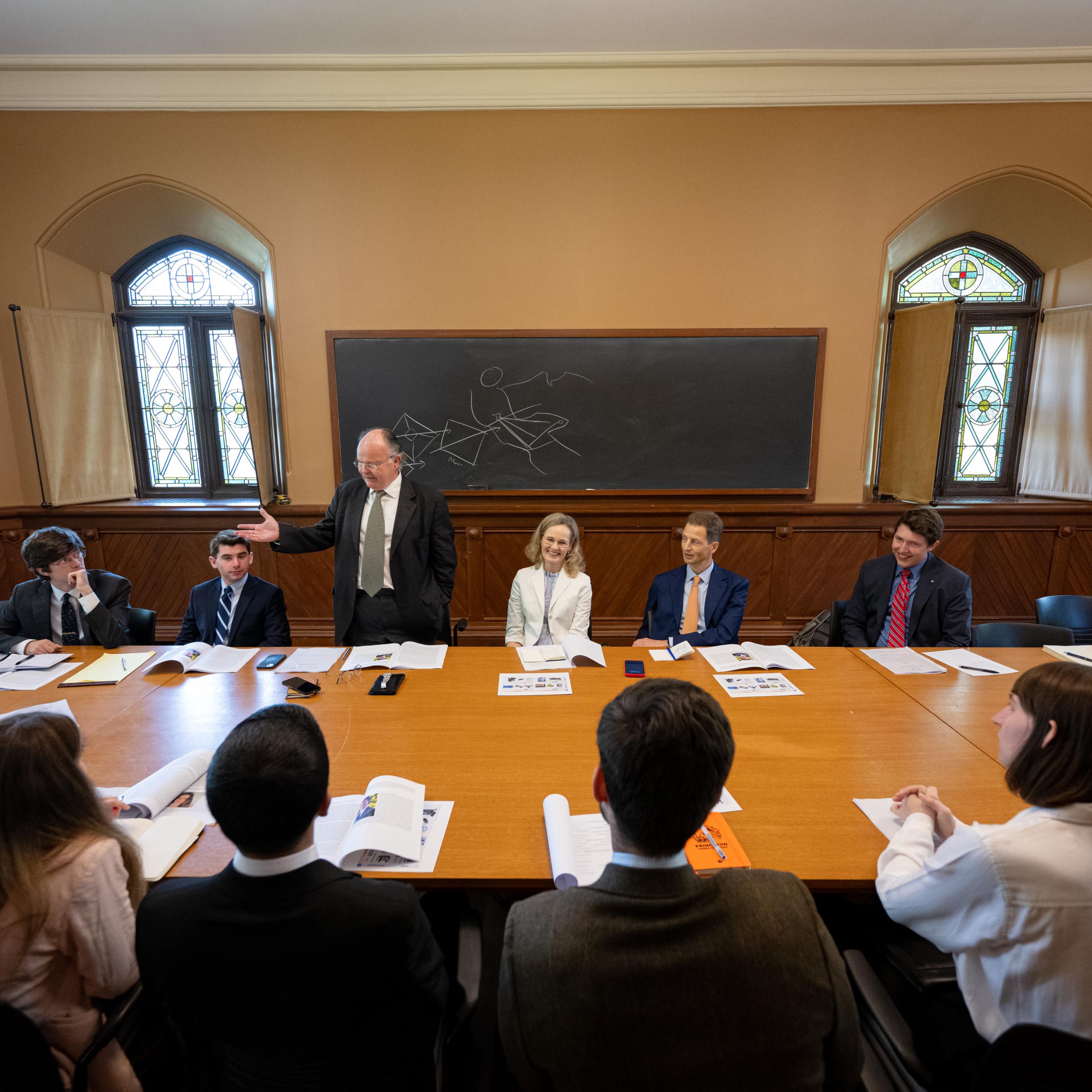 Multiple people sitting around a table with a blackboard in the background.