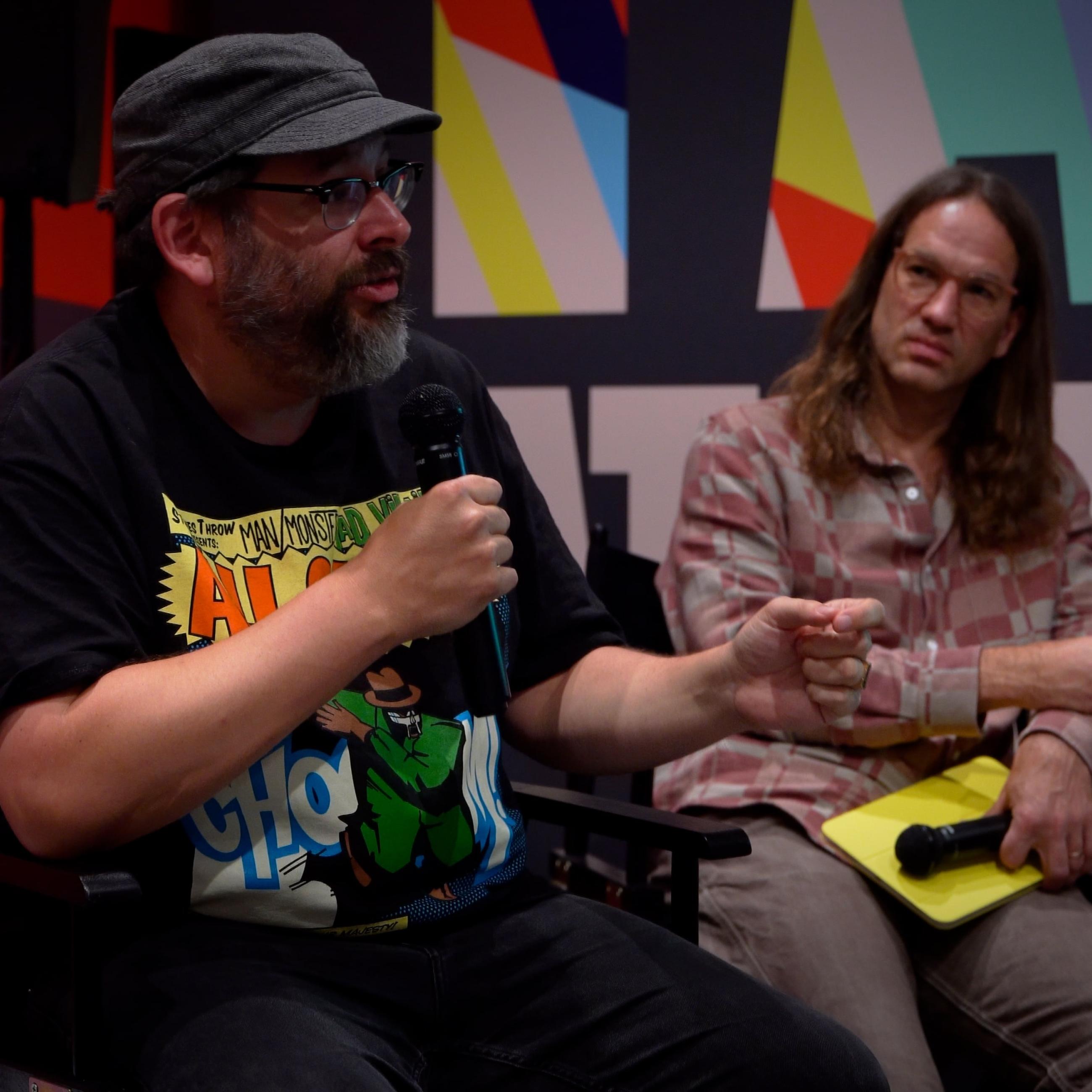 Two men sitting and one is speaking into microphone at Sing for Science